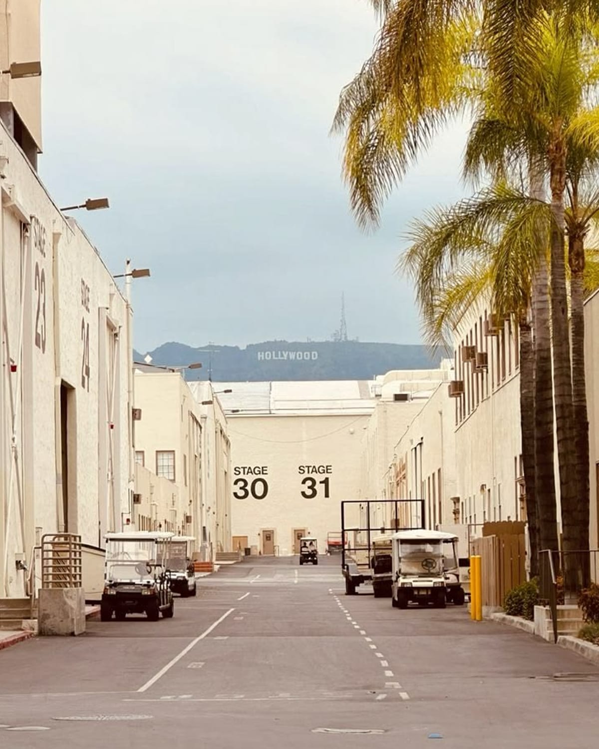 Studio backlot street lined with sound stages, with the Hollywood sign in the distance
